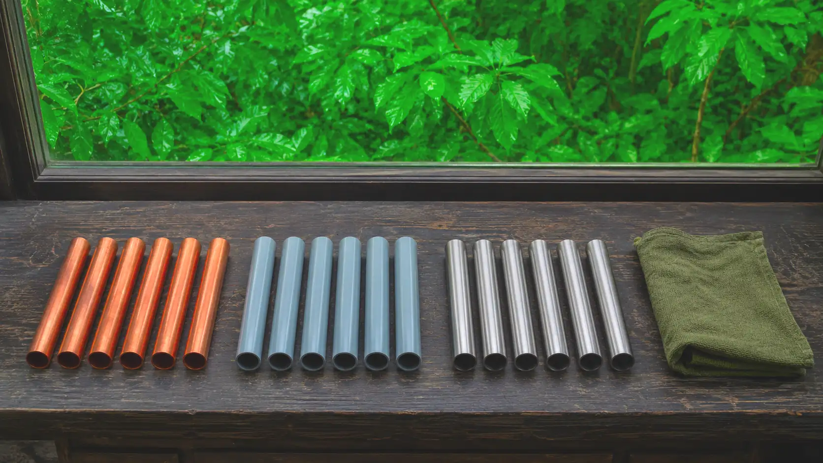Nach Material sortierte Rohrabschnitte aus Kupfer, Kunststoff und Edelstahl auf einer dunklen Holzwerkbank am Fenster