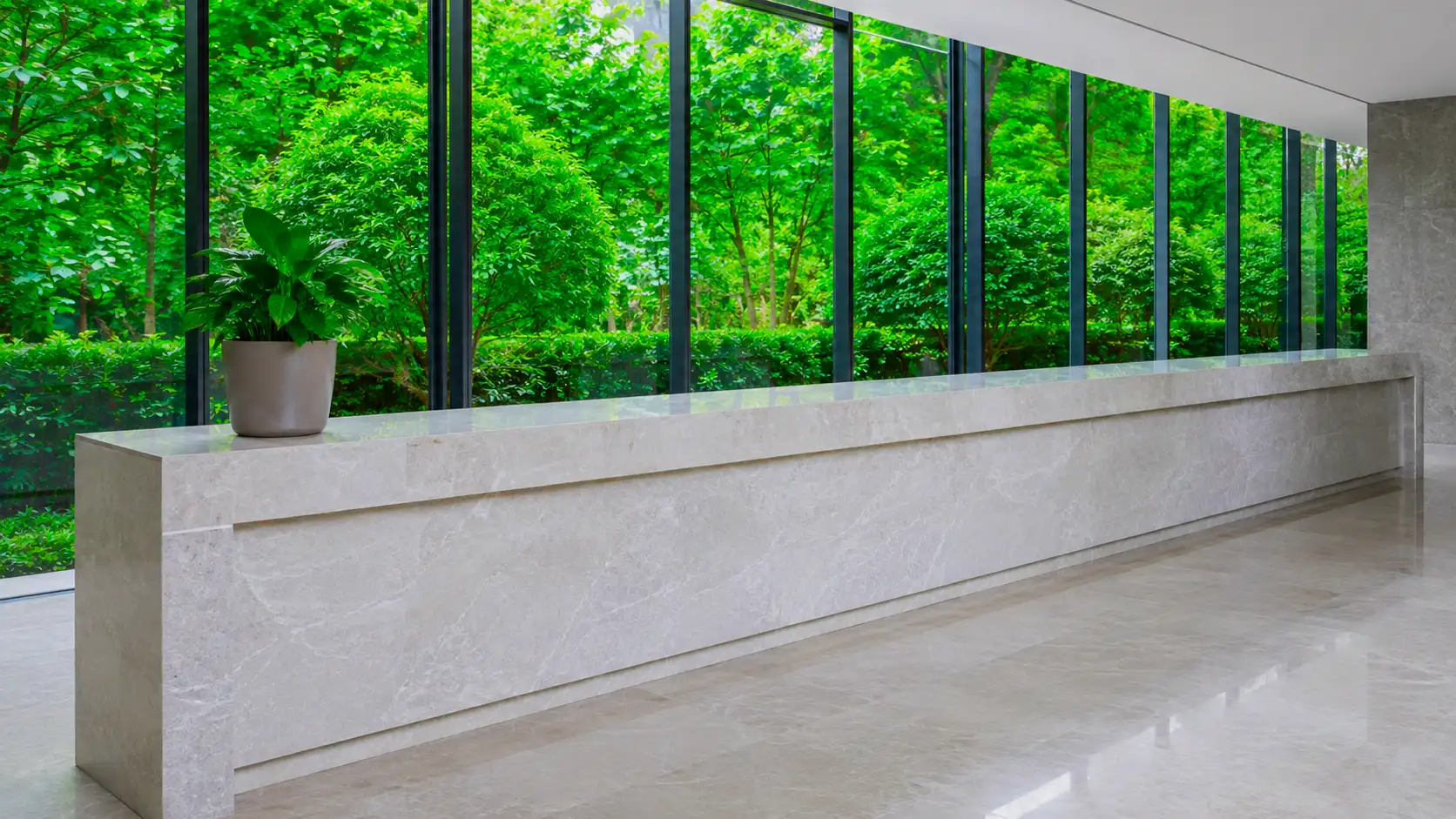 A long empty stone counter in a bright room, a glass wall onto greenery behind